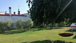 A grassy yard with trees, a swing, and a building with chimneys in the background. - Apartments Tara Apt 2 (Medulin)