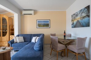 A living room with a blue sofa, a glass table with chairs, a painting, and a wooden cabinet. - Apartments Tara Apt 2 (Medulin)