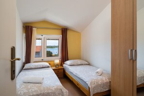 A bedroom with two single beds, a window with curtains, and a view of a building outside. - Apartments Tara Apt 2 (Medulin)