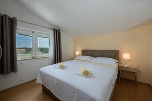 A hotel room with a bed, two bedside lamps, a window with curtains, and a view of the outside. - Apartments Tara Apt 2 (Medulin)