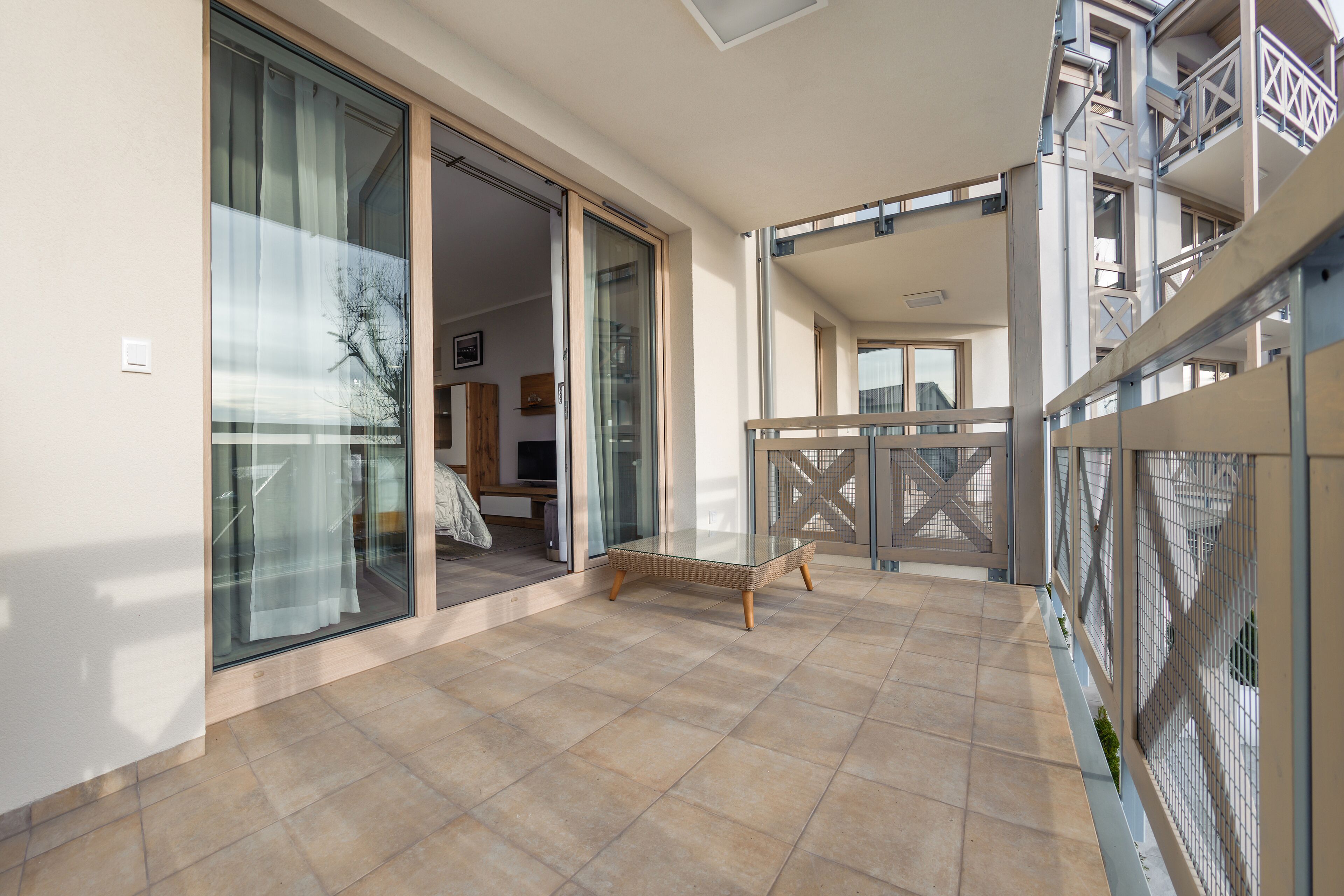 Ein Balkon mit einem Korbstuhl-Tisch, einer Glast ür zu einem Innenraum und Blick auf ein Gebäude gegenüber.