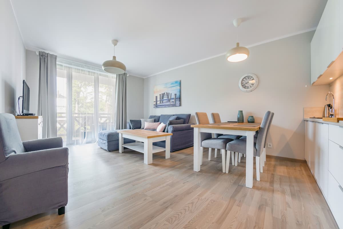 Una sala de estar moderna con sofá, mesa de centro y mesa de comedor. Hay un televisor, un cuadro y un reloj en la pared.