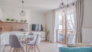 A modern kitchen with a dining area, a TV, and a large window with curtains. - Apartamenty Sun&Snow Rezydencja Park (Mielno)