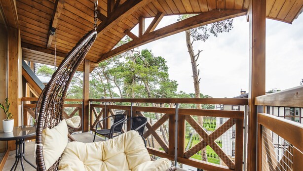 A wooden deck with a hanging chair, a small table with a plant, and a view of a green landscape. - Apartamenty Sun&Snow Rezydencja Park (Mielno)