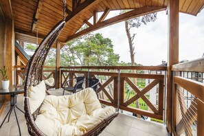 Une terrasse en bois avec un fauteuil suspendu, une petite table agrémentée d’une plante, et une vue sur un paysage verdoyant.