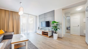 A modern living room with a flat-screen TV, a sofa, a coffee table, and a large potted plant. - Apartamenty Sun&Snow Rezydencja Park (Mielno)