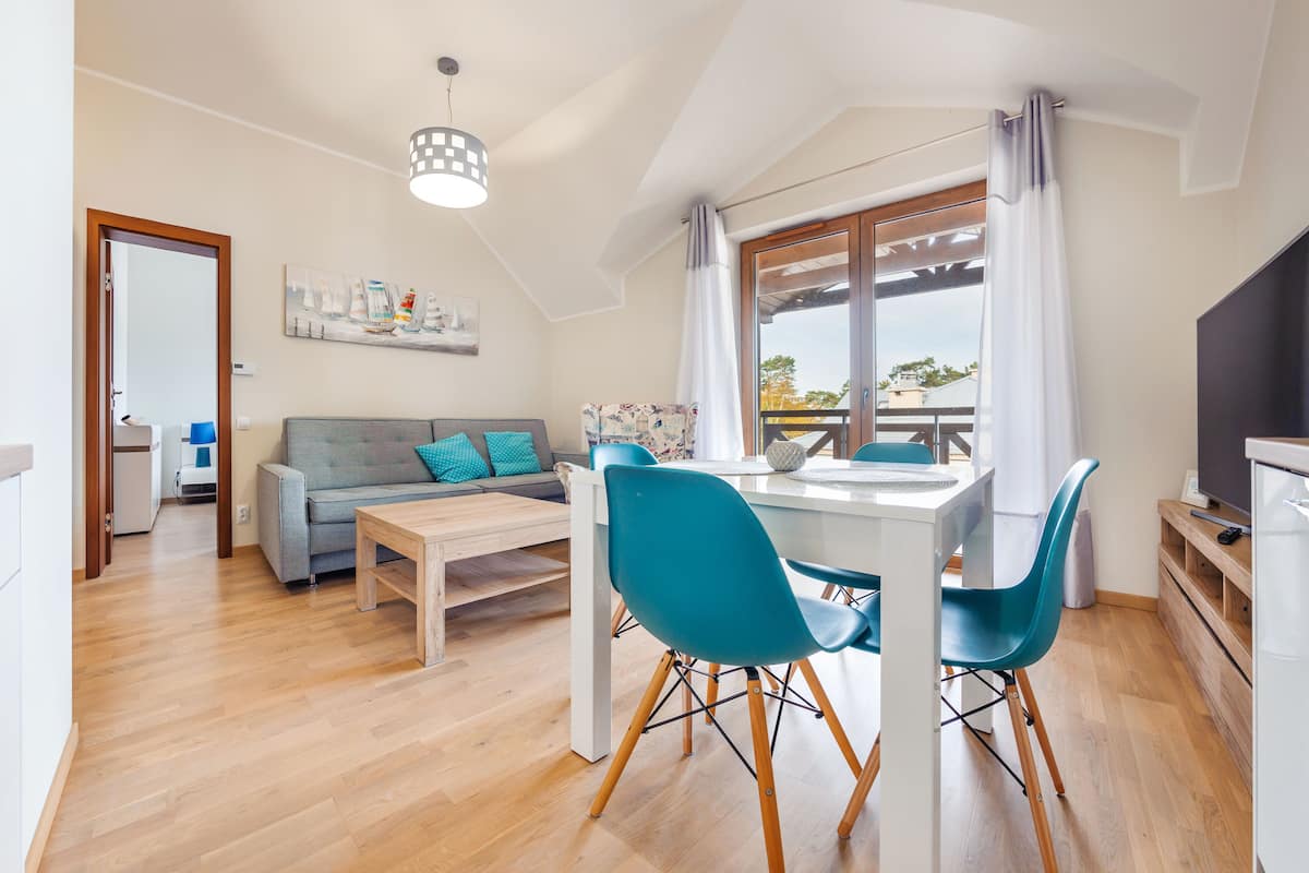 Una sala de estar moderna con un sofá, una mesa de comedor con sillas, un televisor y un balcón con vistas.