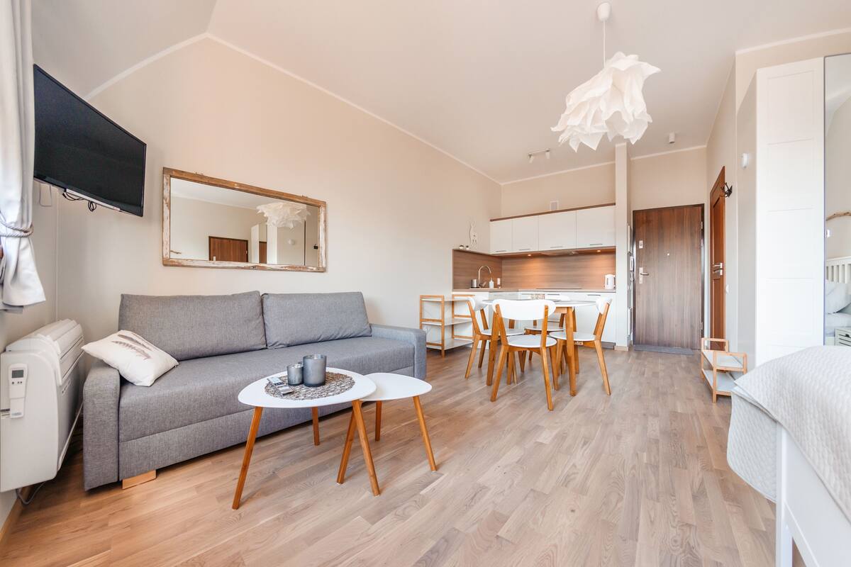 Una sala de estar moderna con un sofá gris, una mesita redonda y una zona de comedor con sillas de madera y una mesa blanca.
