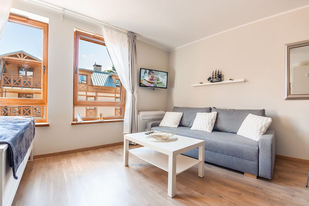 Una sala de estar moderna con un sofá gris, una mesa de centro blanca y piso de madera.