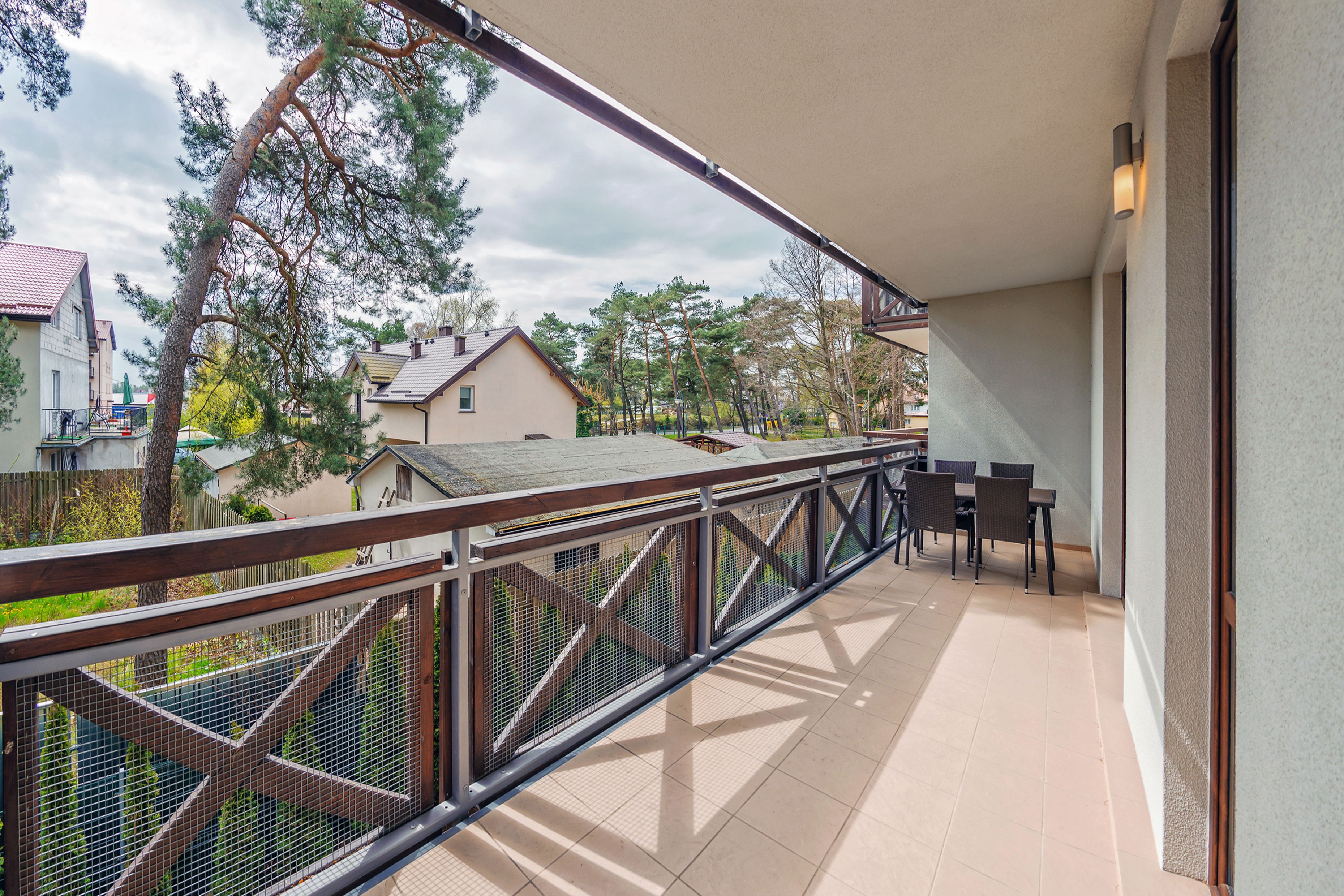 A balcony with a metal railing, a table with chairs, and a view of houses and trees in the background.