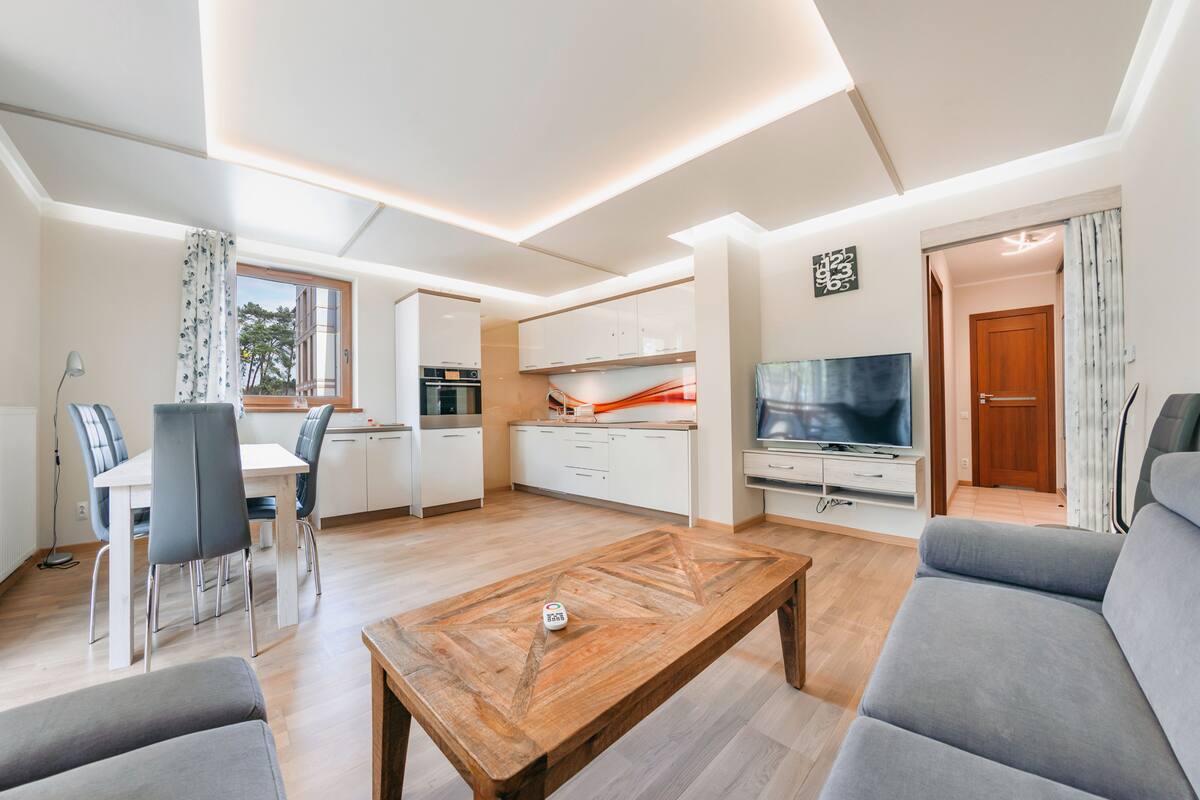 Una sala moderna con una mesa de centro de madera, un sofá gris y un televisor.
