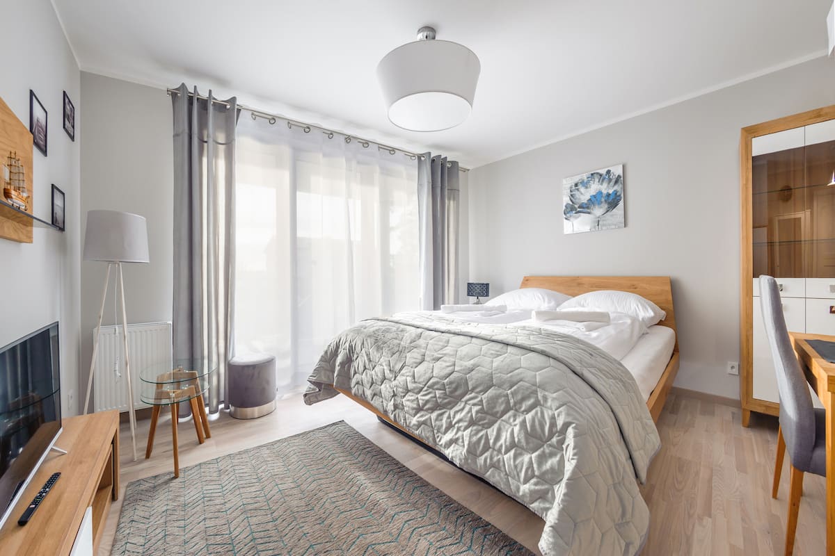 Un dormitorio moderno con cama, mesita de noche, lámpara y vistas a un paisaje urbano a través de la ventana.
