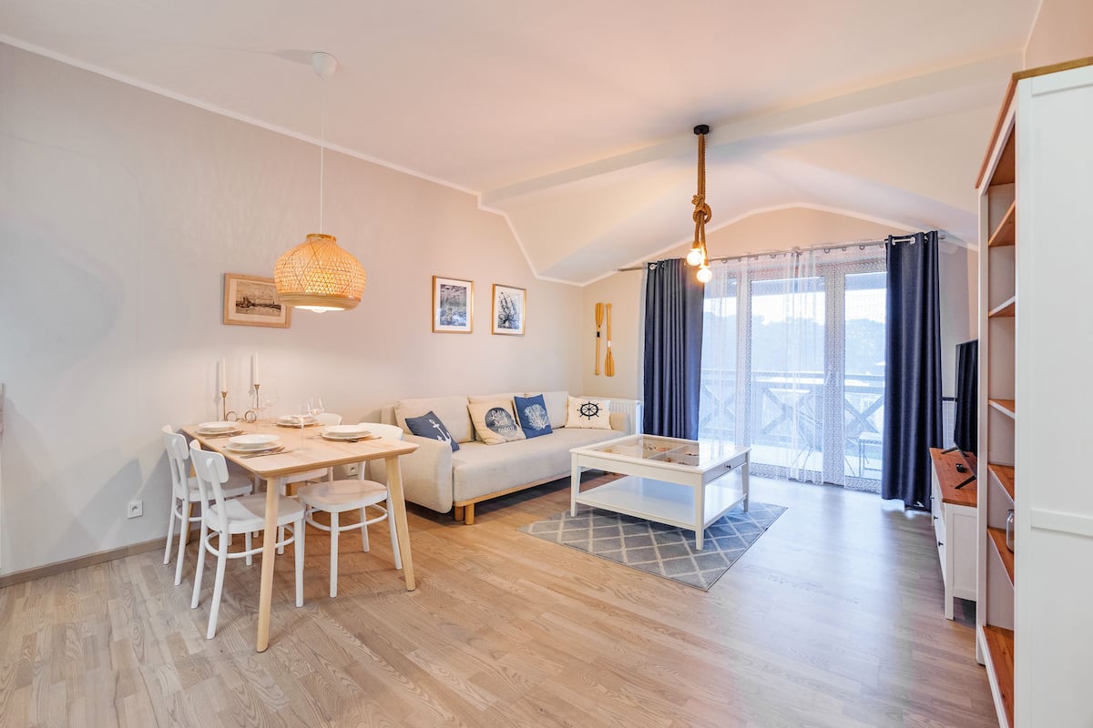 Un salón moderno y bien iluminado con una mesa de comedor, sofá y vistas al exterior a través de amplios ventanales.