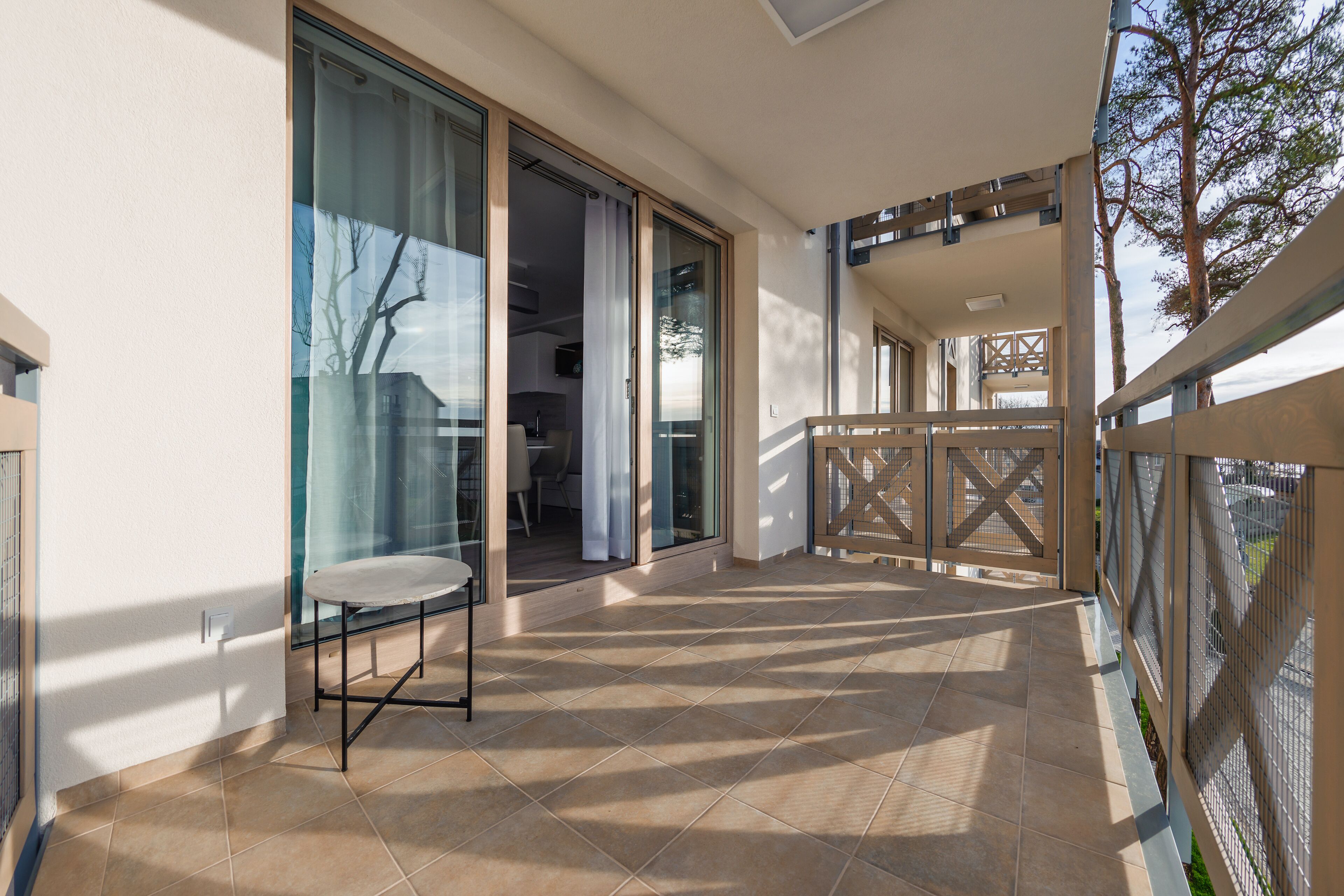 A balcony with a table and chairs, large glass doors leading to an interior room, and a view of the outside.