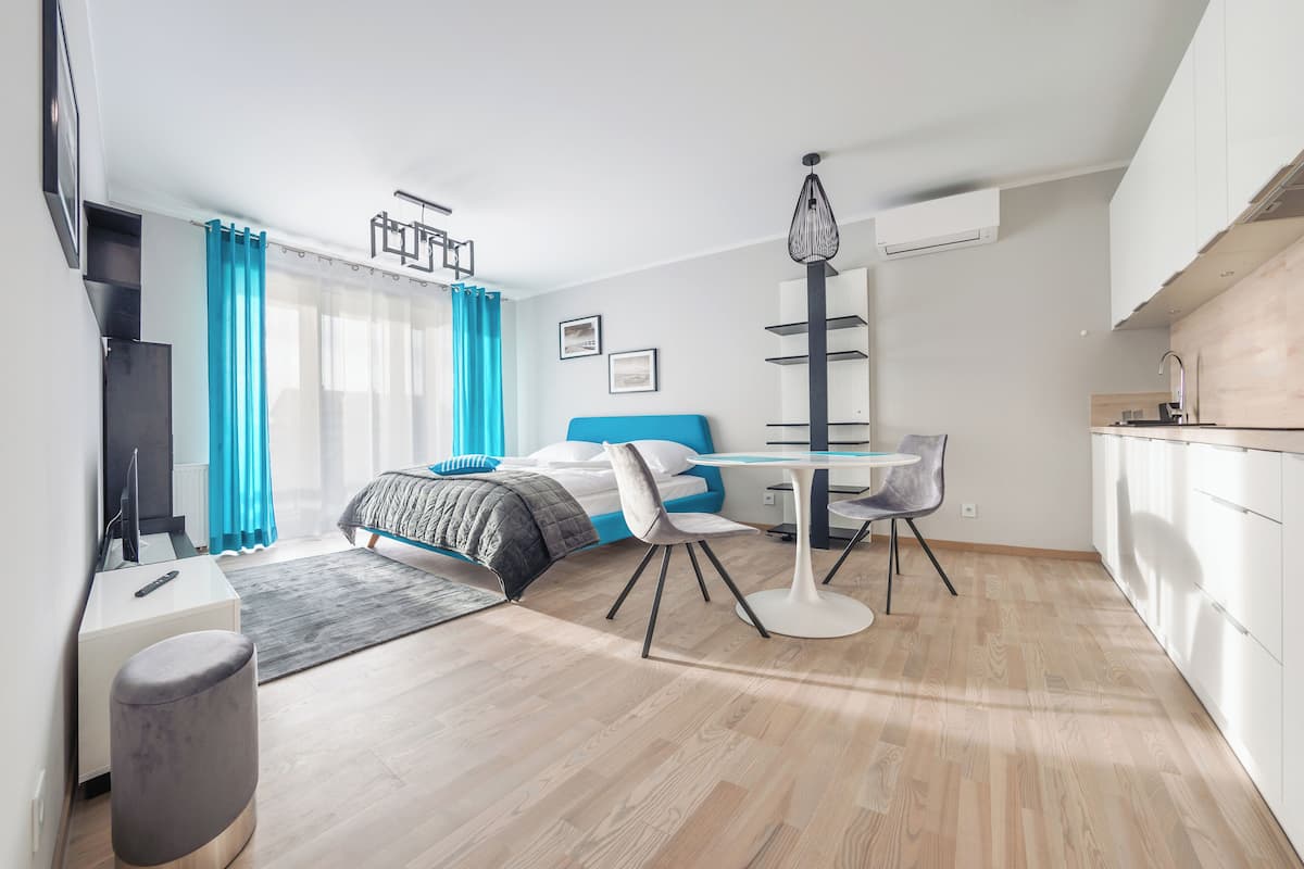 Una habitación de hotel moderna con cama, escritorio, silla, mesita y kitchenette.