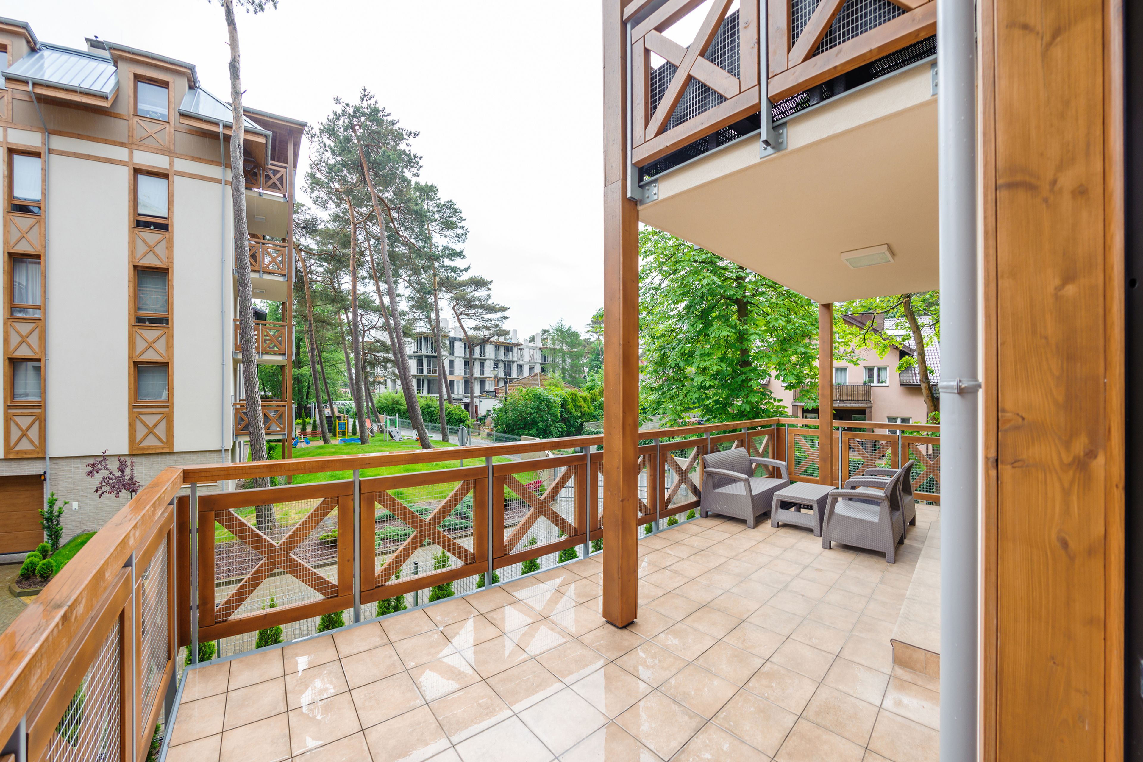 Eine überdachte Terrasse im Freien mit Fliesenboden, Holzgeländern und Gartenmöbeln.