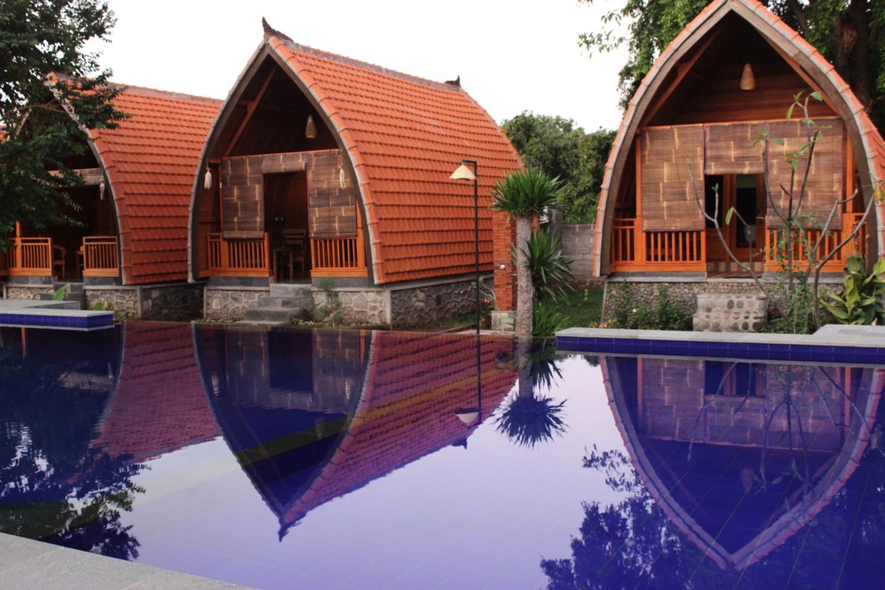 Um edifício com um design de telhado em arco distinto, uma piscina refletora à frente e uma base de pedra.
