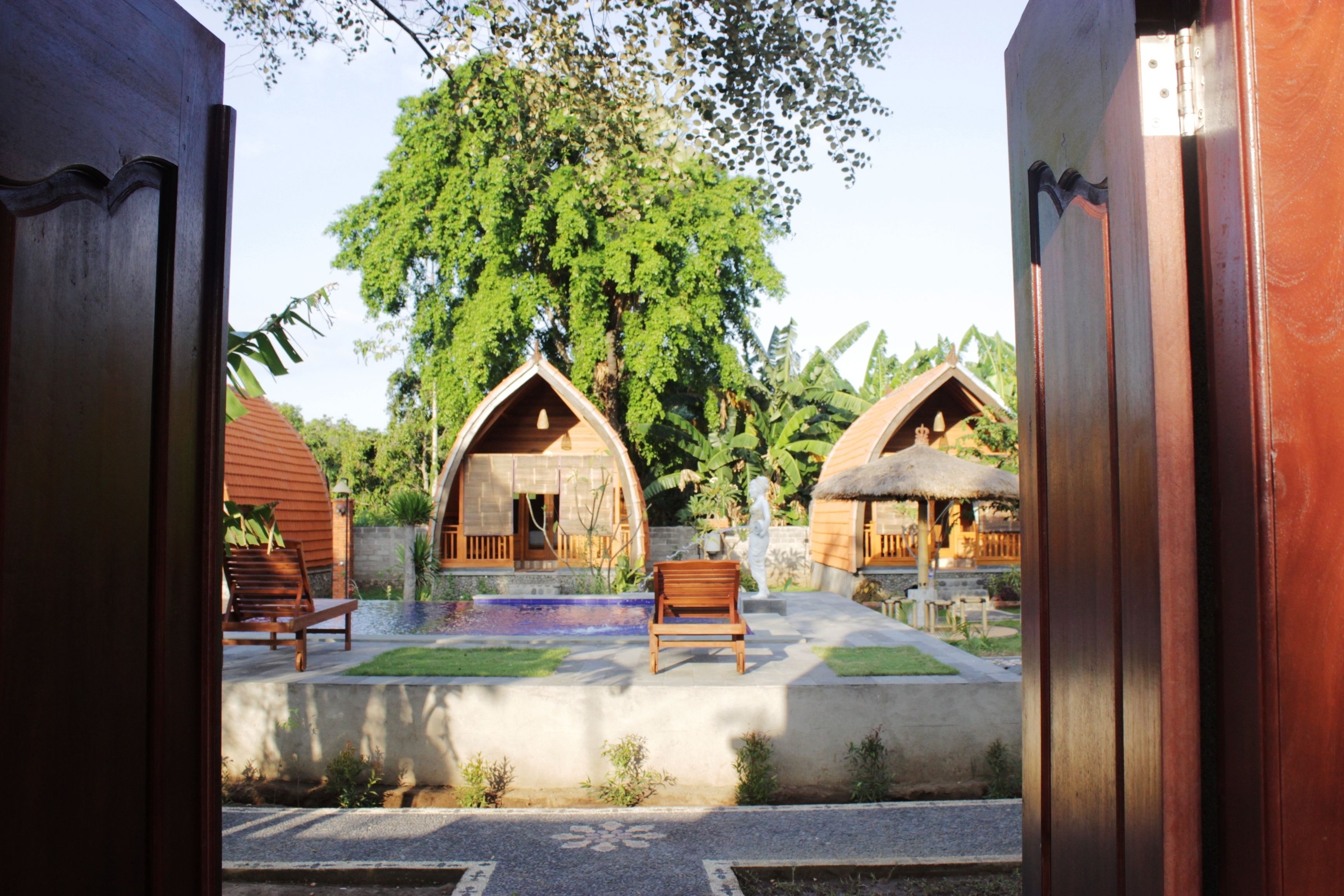 A courtyard with wooden huts, benches, and a central tree.
