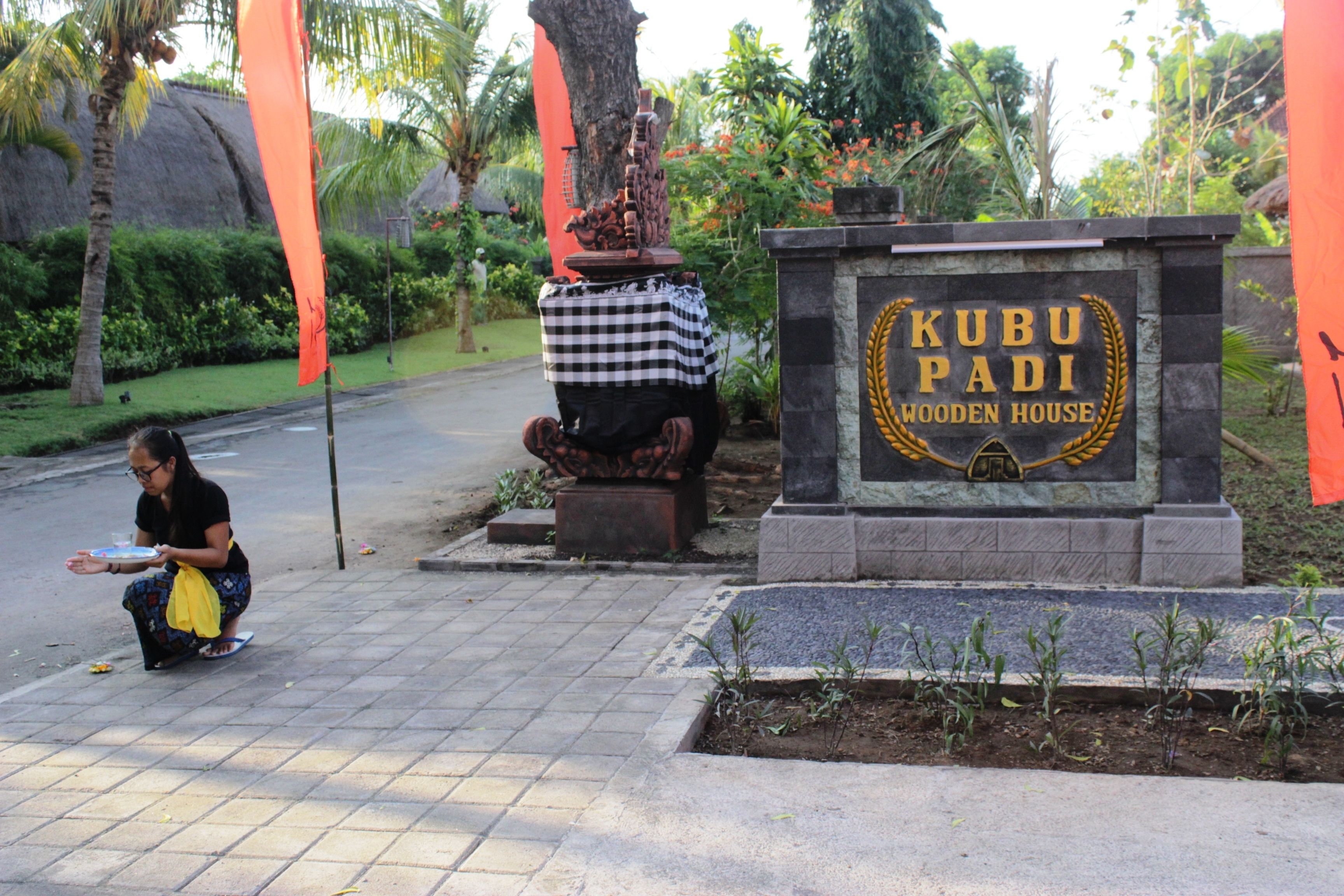 A sign for Kubu Padi Wooden House with a checkered cloth on a pedestal.