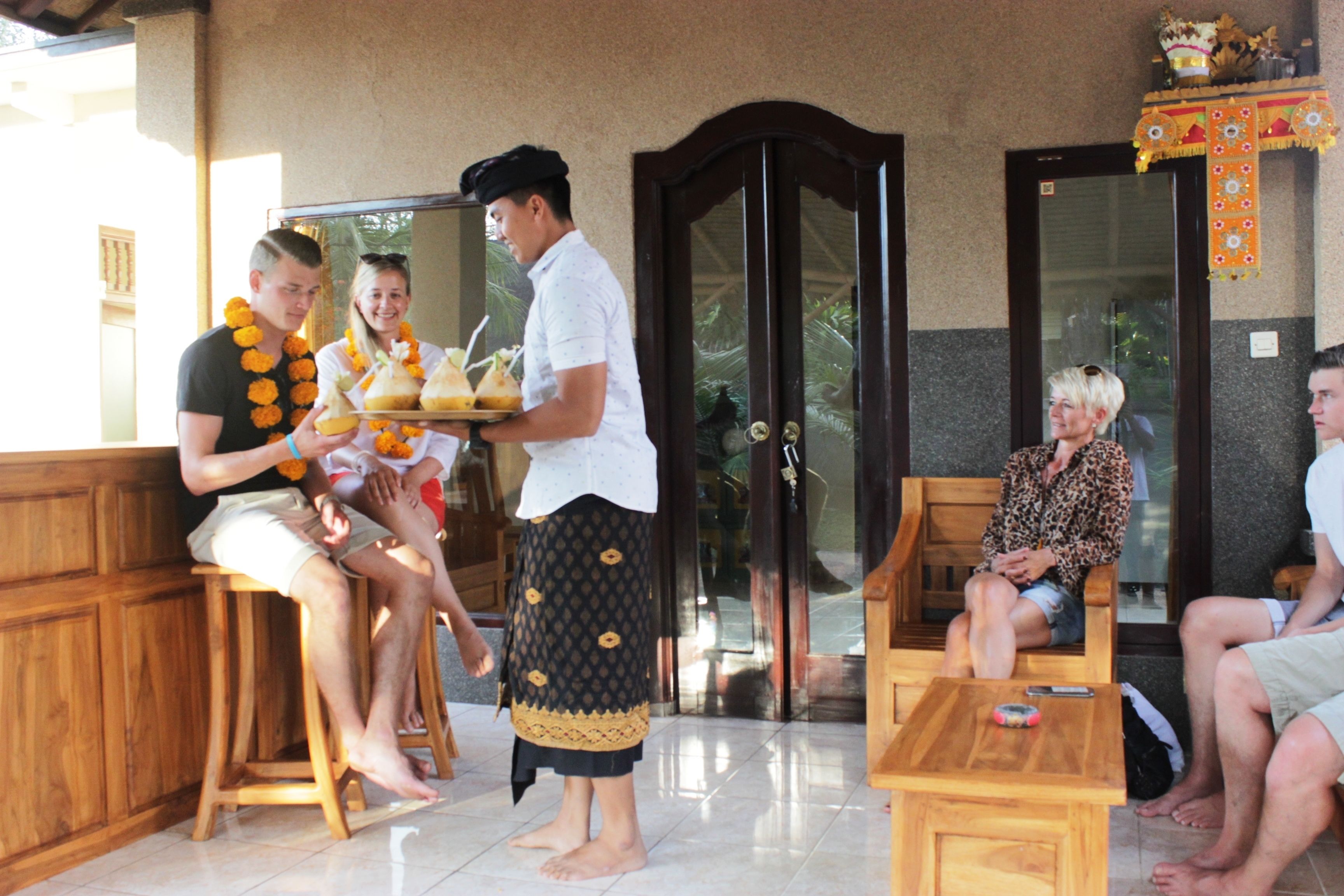 A traditional ceremony with participants seated and standing, a wooden bench, and a table with a remote control.