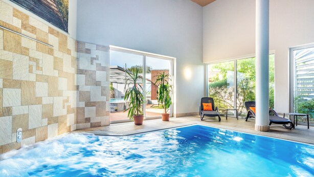 En indendørs swimmingpool med krystalklart vand, omgivet af fliserede vægge og plantekasser.