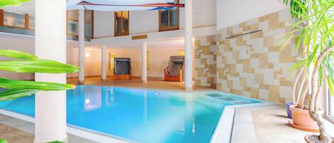 An indoor swimming pool with a tiled floor, a ceiling with a white canopy, and potted plants.