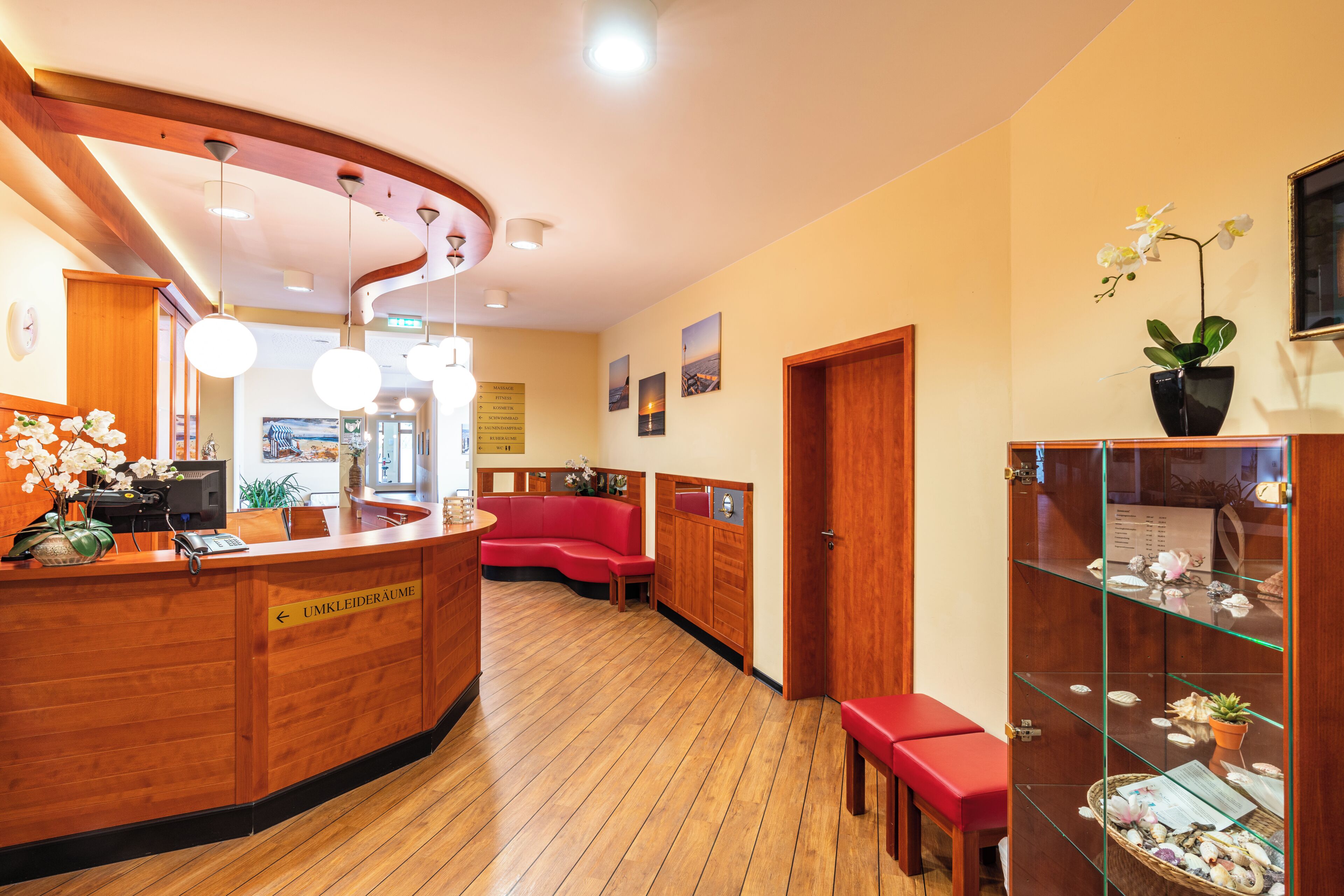 A reception area with a wooden reception desk, a red sofa, and a glass display cabinet with decorative items.