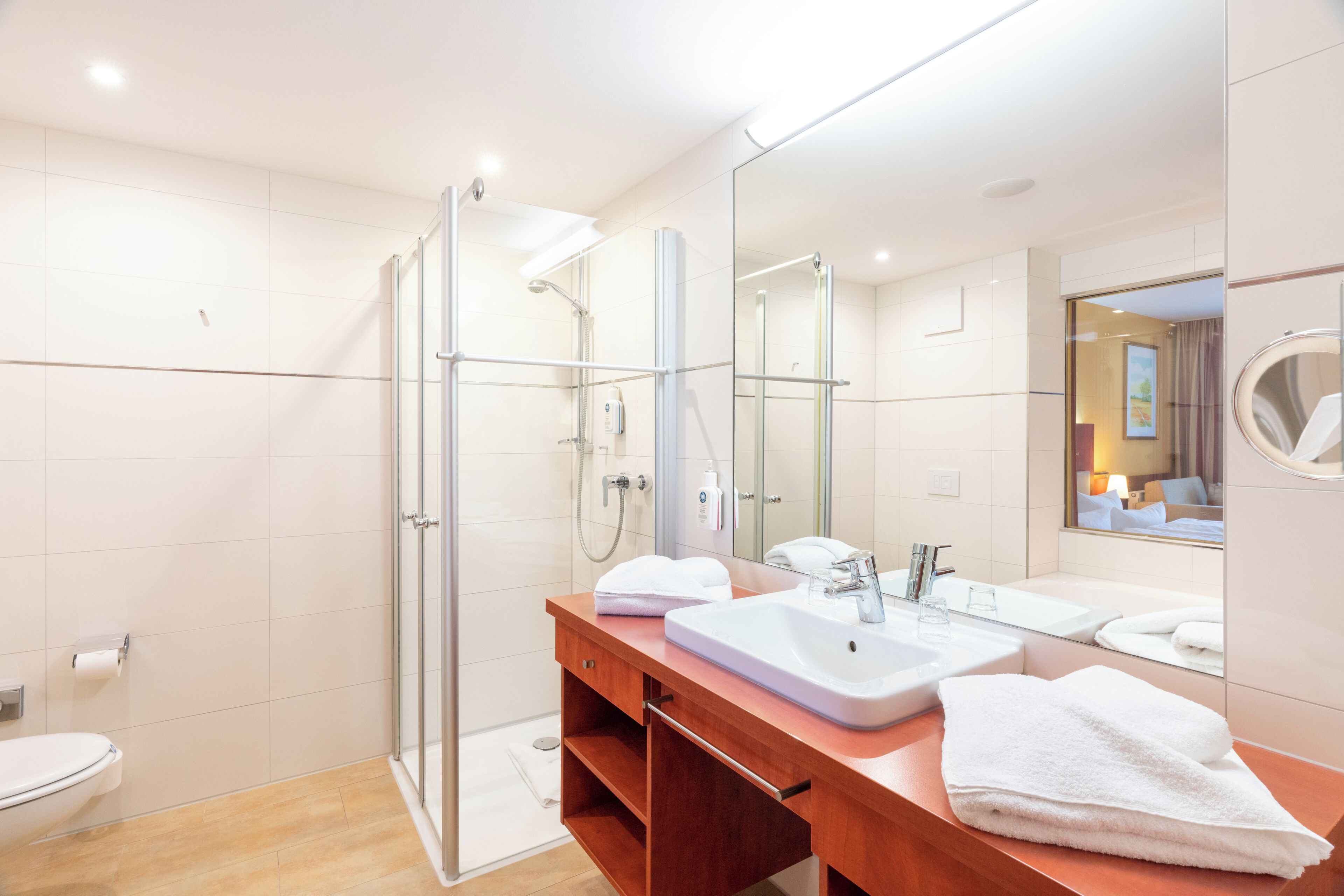 Un baño moderno con cabina de ducha de vidrio, tocador de madera con lavabo y un espejo grande.