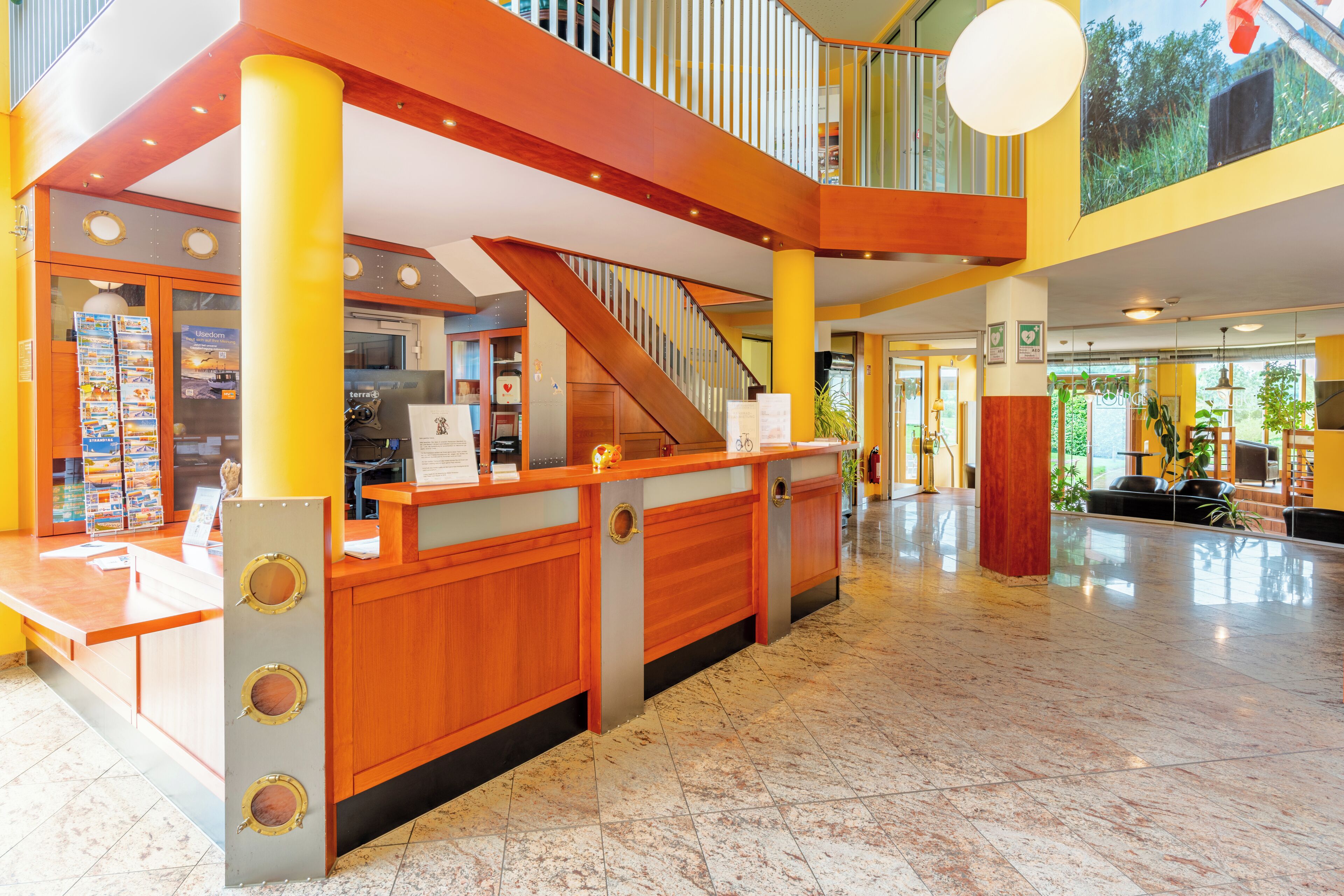 A hotel lobby with a reception desk, a staircase, and a high ceiling with natural light.