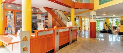 A hotel lobby with a reception desk, a staircase, and a high ceiling with natural light.