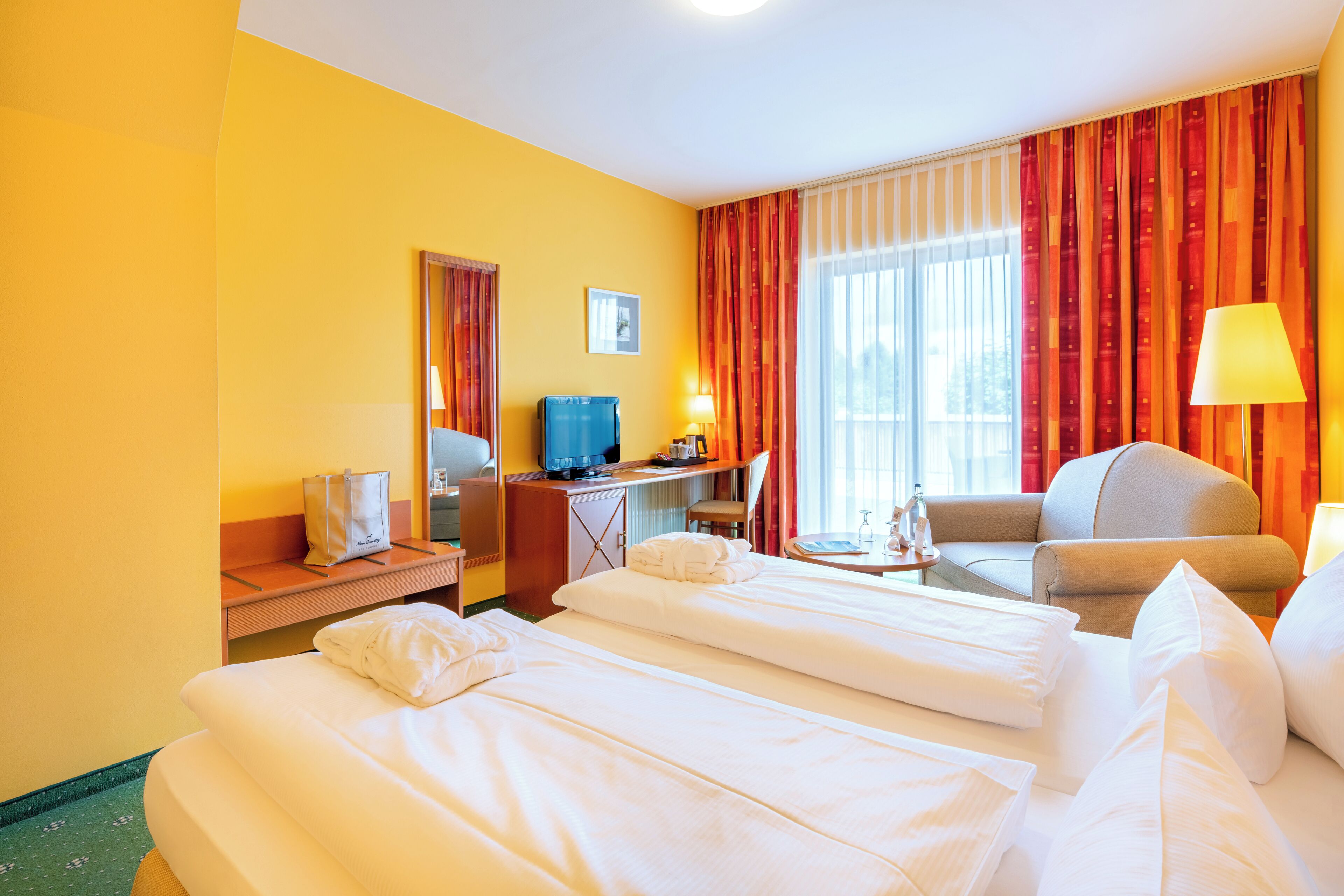 Habitación de hotel con dos camas, un escritorio, una silla, un televisor y una ventana con cortinas.