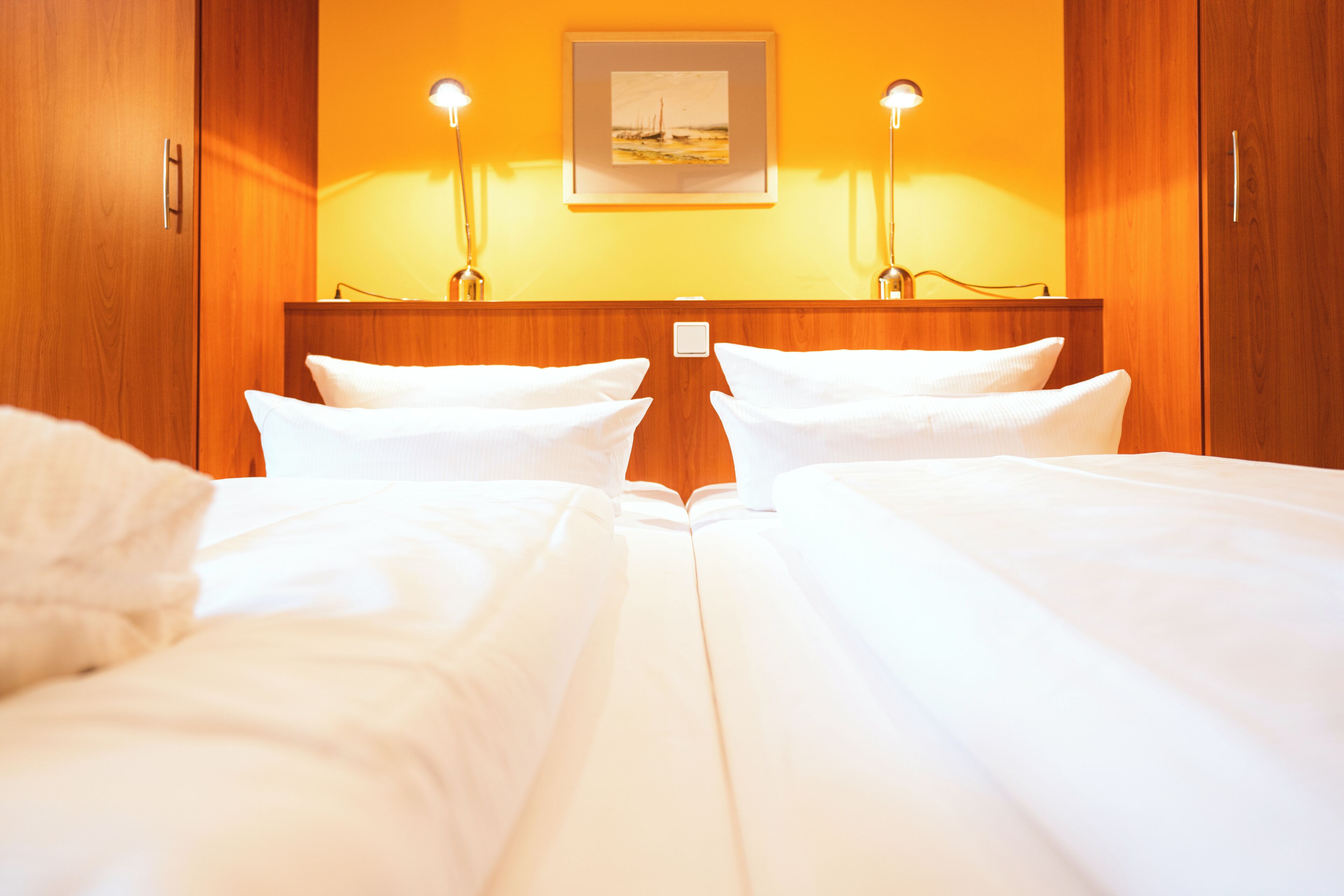 A hotel room with two beds, wooden wardrobe, and a painting on the wall.