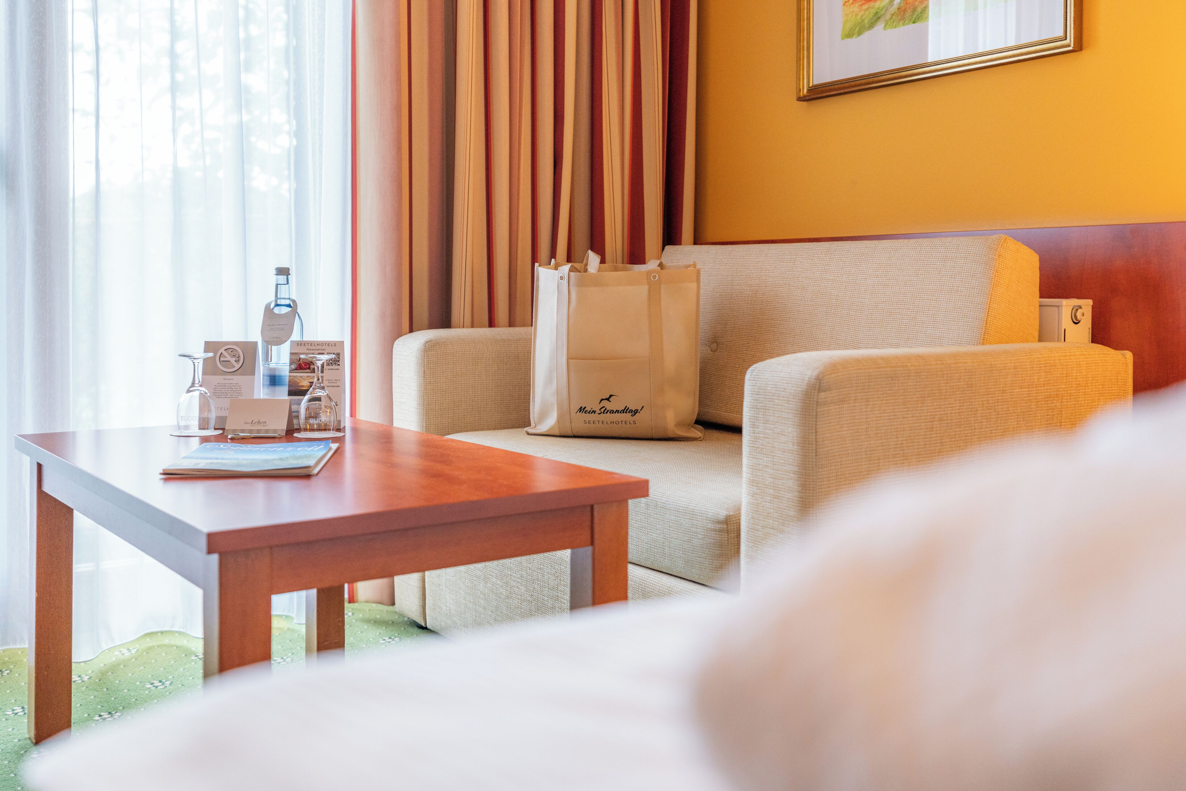 Ein Hotelzimmer mit einer Couch, einem Holztisch und einer weißen Tasche mit einem Logo.