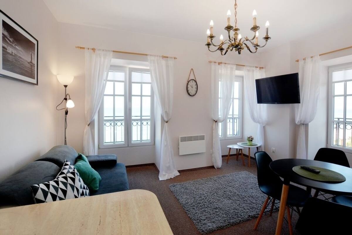 Ein gut beleuchteter Raum mit einer Couch, einem Esstisch mit Stühlen, einem Fernseher und einer Kristallleuchtre.