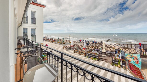 A seaside terrace with outdoor seating, a mural, and a view of the ocean. - Apartamenty Sun&Snow Zachód Slonca (Mielno)
