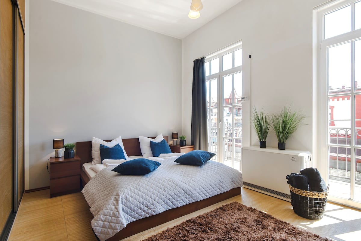 Ein Schlafzimmer mit einem großen Bett, einem Nachttisch, einem Fenster mit Vorhängen und einer Heizung.