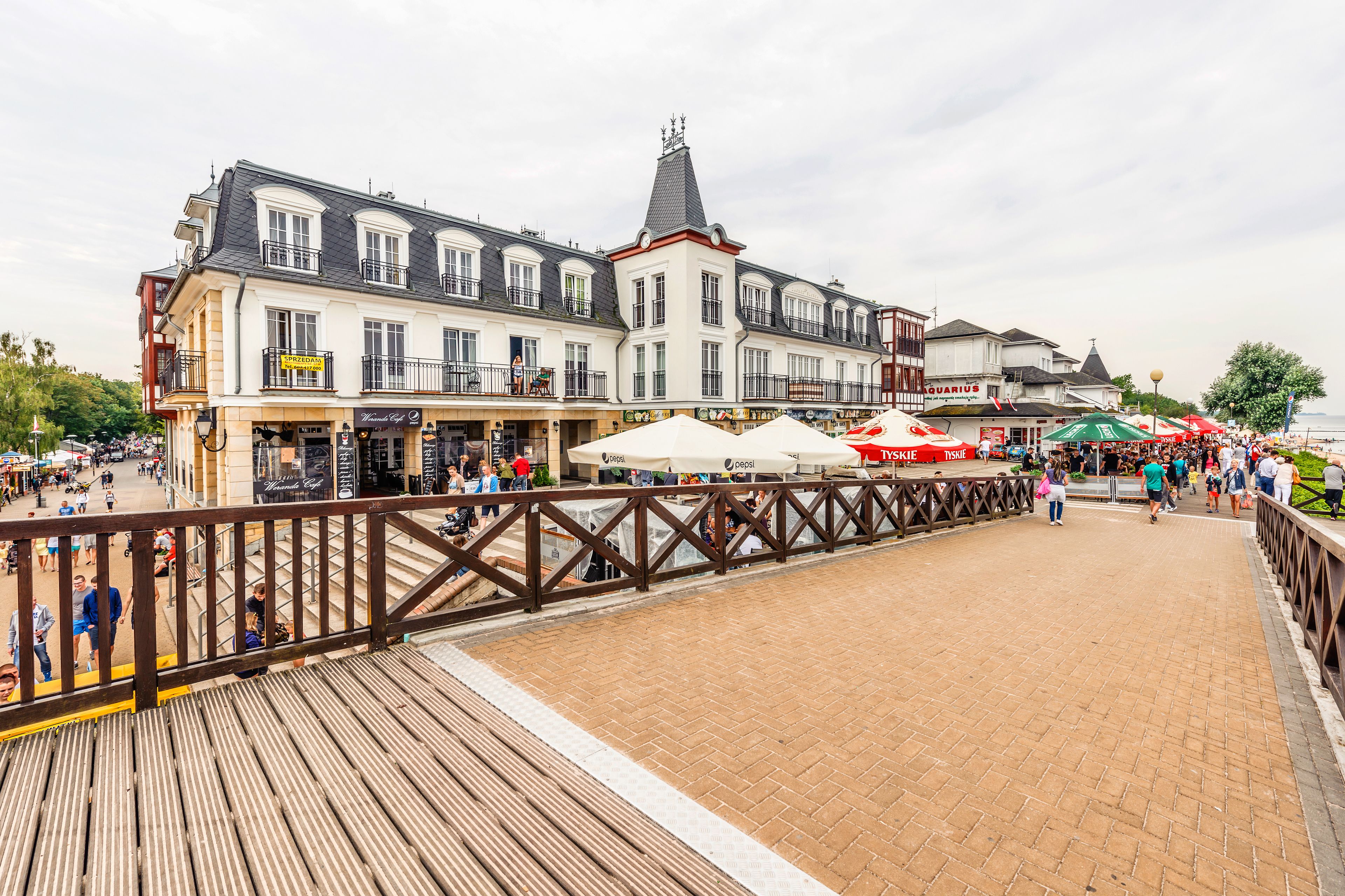 A wooden boardwalk with shops and cafes, a bridge, and a view of the water.