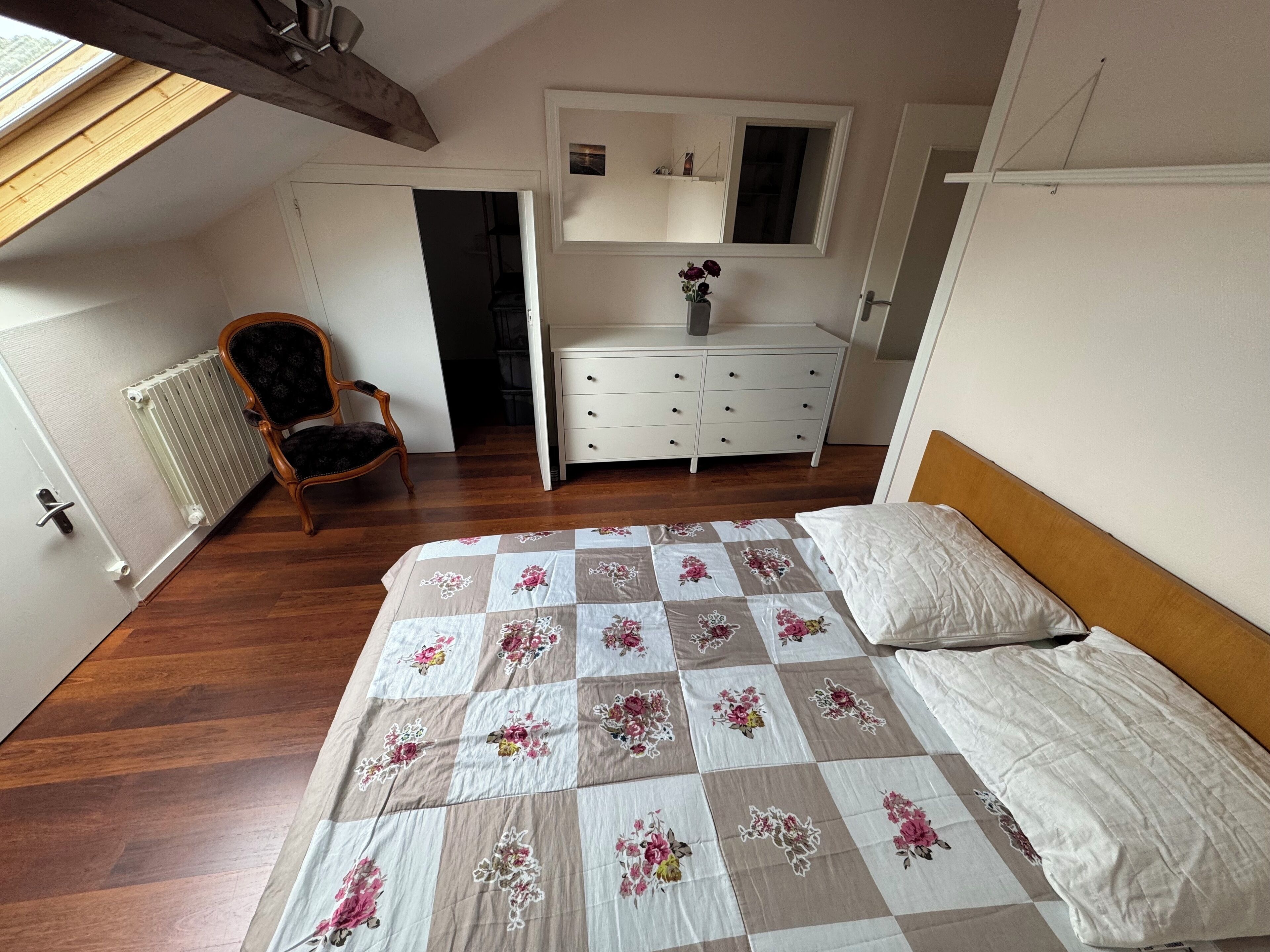 A bedroom with a bed, a chair, a dresser, and a skylight.