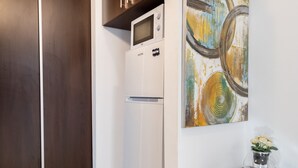 A kitchen with dark wooden cabinets, a white refrigerator, and a wall-mounted microwave. There is a small table with a vase of flowers. - Studio 37 by MRG Apartments (Bucharest)