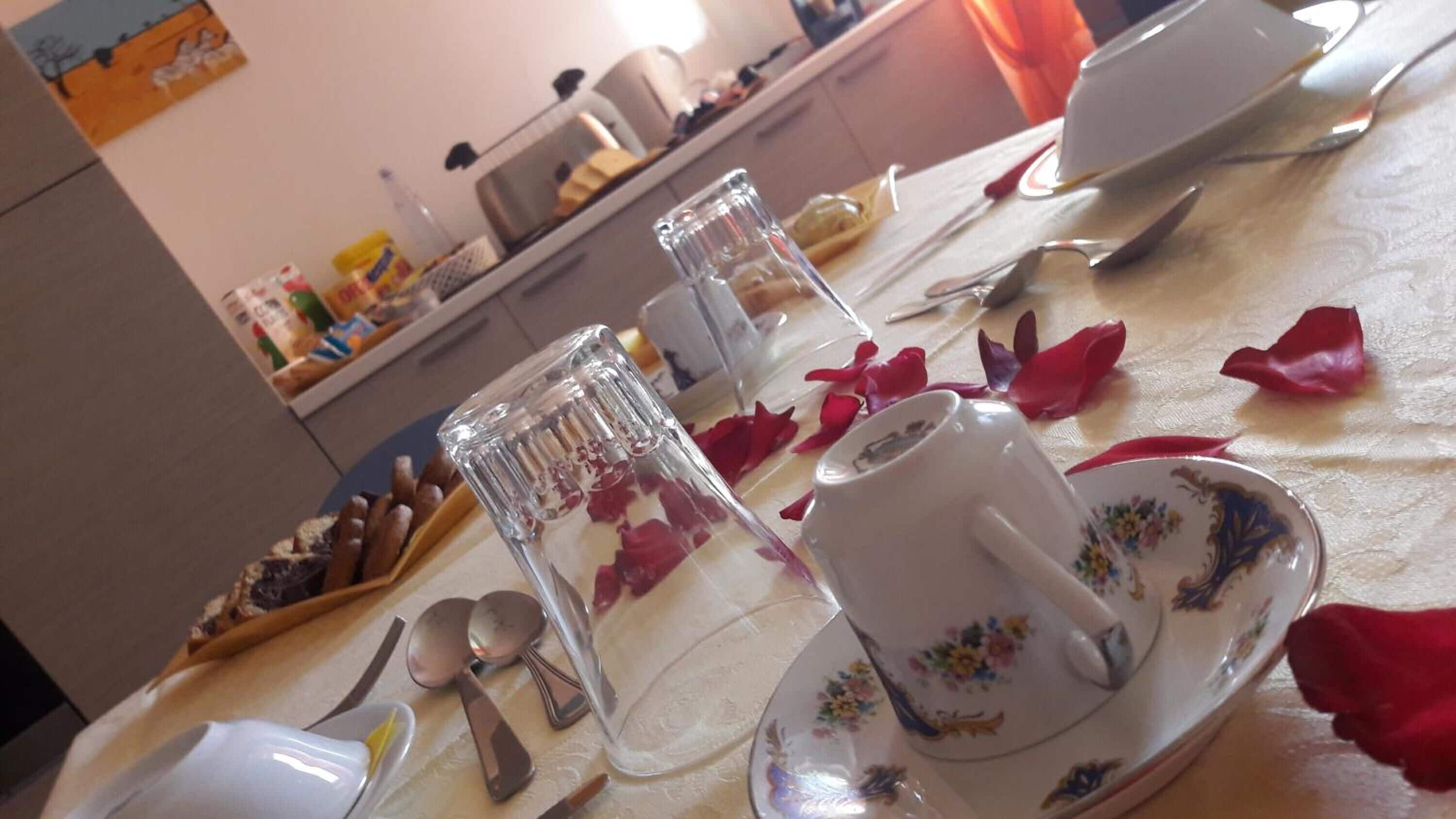 A dining table set with plates, cups, and cutlery, with rose petals scattered on the tablecloth.