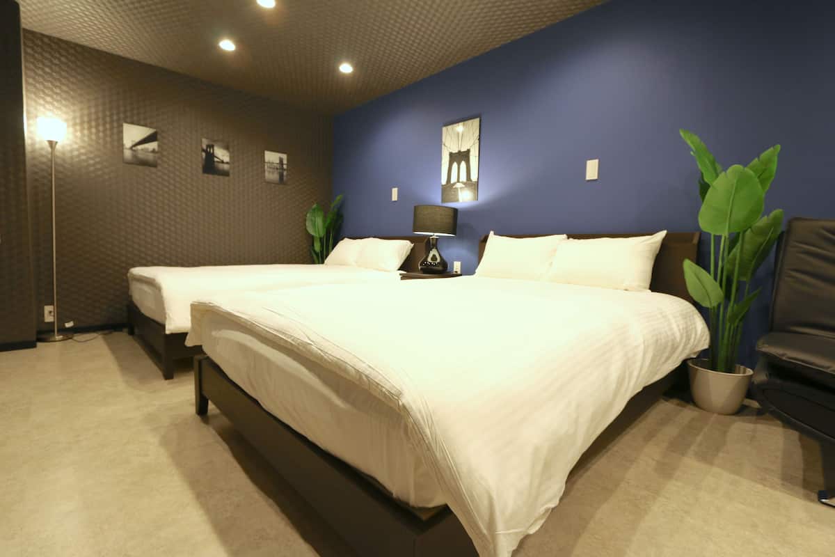 Quarto de hotel com duas camas, mesa de cabeceira, abajur, planta em vaso e parede com quadros.