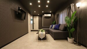 A modern living room with a sofa, a coffee table, a TV mounted on the wall, and a potted plant. - Elizabeth Garden Shinmachi (Osaka)