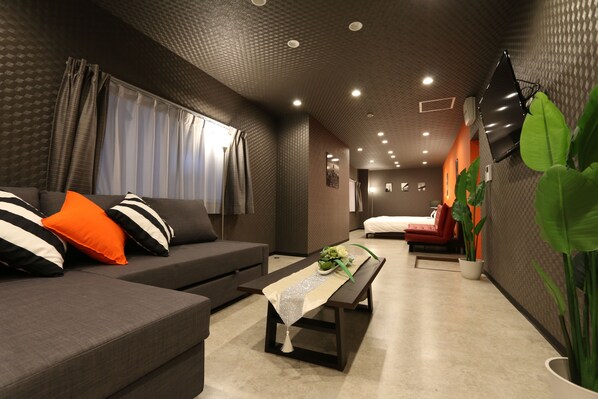 A modern living room with a sofa, a bench, and a flat-screen TV mounted on the wall. - Elizabeth Garden Shinmachi (Osaka)