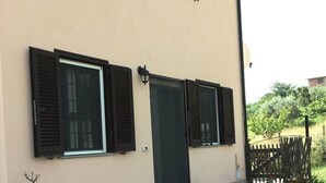 A building with a beige facade, three windows with shutters, a door, and a row of potted plants along the front. - Terra Luna house in the countryside (Mentana)