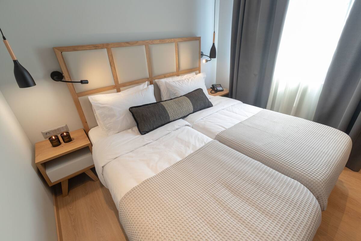 Una cama doble con cabecera de madera, dos mesitas de noche, una lámpara y un teléfono a un lado.