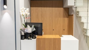 Una mesa de recepción con un reloj encima, un panel de madera y un jarrón con flores.
