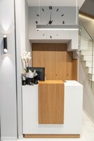 Ein Empfangsschalter mit einer darüber hängenden Uhr, einer Holzwand und einer Vase mit Blumen.