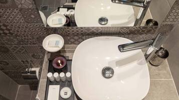 A bathroom with a white sink, chrome faucet, and a mirror above it. There are toiletries on the counter, including a soap bar, a candle, and a small container.