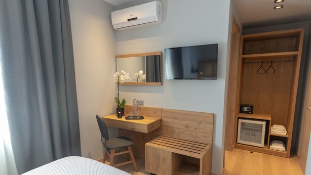 Habitación de hotel con cama, escritorio, silla, televisión, armario y un refrigerador pequeño.
