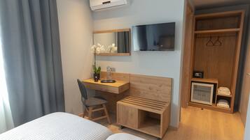 A hotel room with a bed, a desk, a chair, a TV, a wardrobe, and a small fridge.